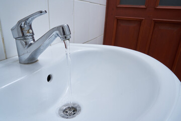 metallic faucet with running water in a white bathroom