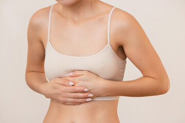 young woman in beige underwear holds her stomach with her hands, feels pain, isolated on a beige...