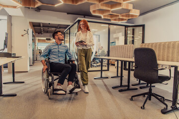 Fototapeta na wymiar Young business colleagues, collaborative business colleagues, including a person in a wheelchair, walk past a modern glass office corridor, illustrating diversity, teamwork and empowerment in the