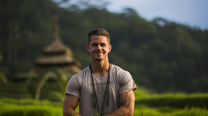 A charismatic male supermodel stands against a scenic backdrop of Balinese countryside and residences, embodying both the allure and charm of nature.
