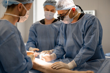 Three confident surgeons performing surgical operation on a patient's knee in operating room....