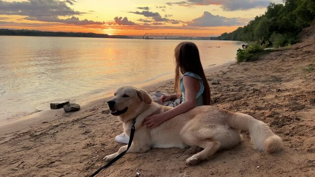 Best friends - a child and a dog sit together, a child leans against the dog, and both enjoy the sunset on the river bank