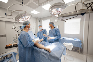 Three confident surgeons performing surgical operation on a patient's knee in operating room....