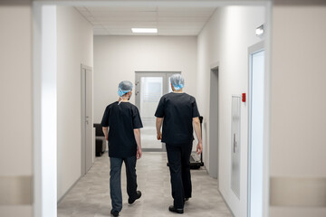 Two surgeons in uniform walk along the corridor of the surgical department, view from a backside