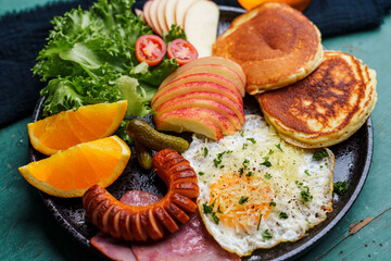 Breakfast pancakes, fried eggs, sausages, ham and fruit.