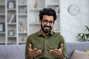 Video call online conversation, Indian man sitting on sofa at home, looking at web camera smiling...