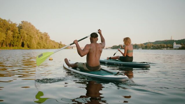 African american couple in activewear swimming on sup boards