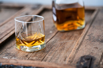 Glass of wiski or scotch on wooden barrel with blurred bottle in background