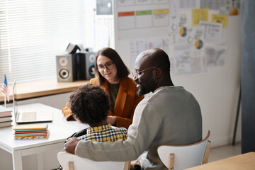 Rear view of African American father talking to teacher about school success of his son