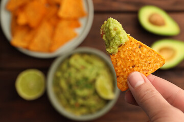 Woman holding delicious nachos chip with guacamole at wooden table, closeup. Space for text