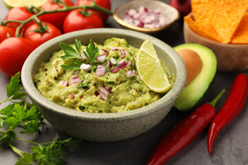 Bowl of delicious guacamole, nachos chips and ingredients on grey table, closeup