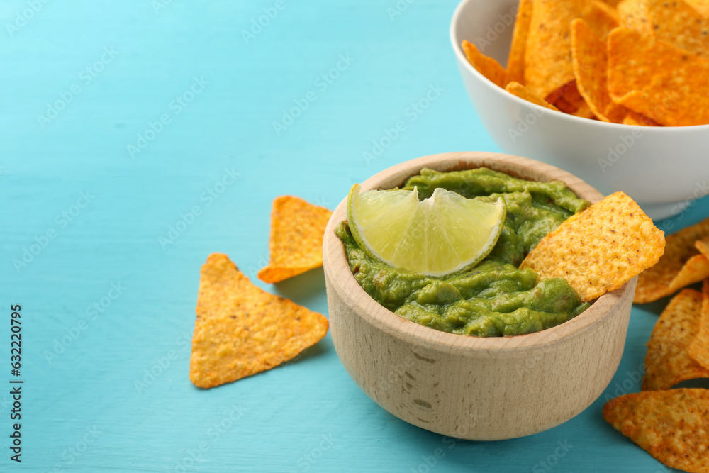 Wall mural bowl of delicious guacamole, lime and nachos chips on light blue wooden table, closeup. space for te