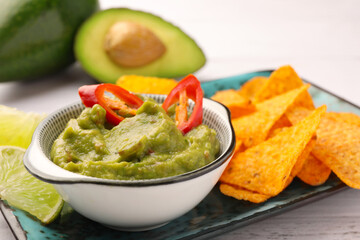 Bowl of delicious guacamole with chili pepper and nachos chips on white wooden table, closeup