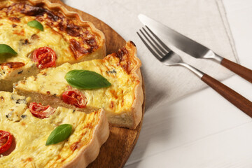 Delicious homemade cheese quiche and cutlery on white wooden table, closeup