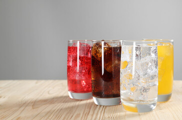 Glasses of different refreshing soda water with ice cubes on wooden table, space for text