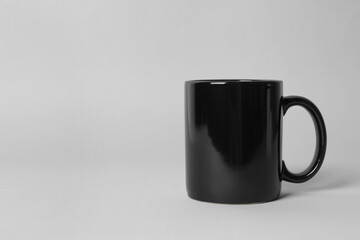 Black ceramic mug on light grey background. Space for text