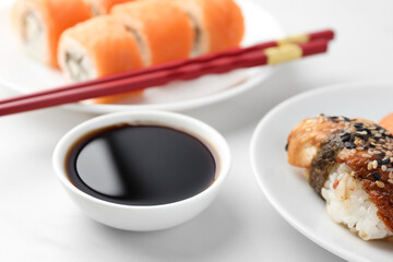 Bowl with tasty soy sauce, chopsticks and different types of sushi on white table, closeup