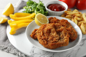 Tasty schnitzels served with potato fries, ketchup and vegetables on marble board, closeup