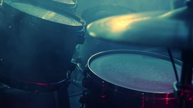 A drummer plays on a dark stage in the fog and neon lights.