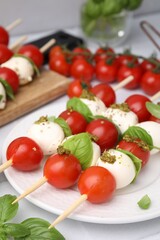 Caprese skewers with tomatoes, mozzarella balls, basil and pesto sauce on table, closeup. Space for text