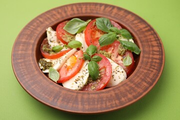 Plate of delicious Caprese salad with pesto sauce on green table, closeup