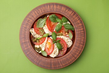 Plate of delicious Caprese salad with pesto sauce on green table, top view