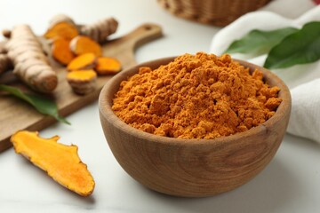 Aromatic turmeric powder and raw roots on white table, closeup