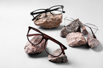 Different stylish glasses on stones against white background