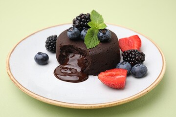 Plate with delicious chocolate fondant, berries and mint on light green table, closeup