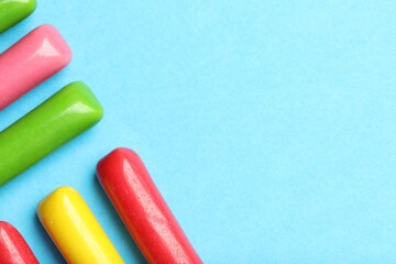 Many tasty bubble gums on light blue background, flat lay. Space for text