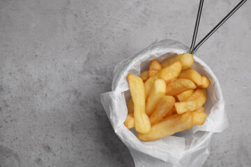 Frying basket with tasty french fries on light grey table, top view. Space for text