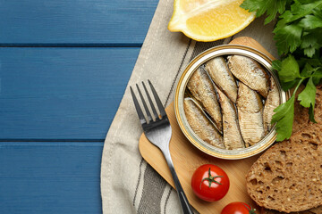 Tin can with tasty sprats served on blue wooden table, flat lay. Space for text