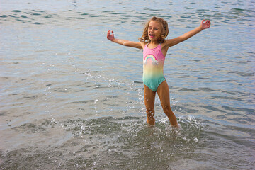 Beautiful happy little girl playing in the waves and splashes on the sea	