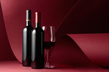 Bottles and glass of red wine on a red background.