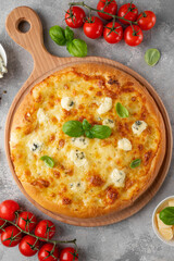 Pizza four cheeses with fresh basil on top on a wooden board on a gray concrete background. Top view, copy space.