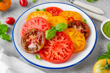 Salad of colorful juicy tomatoes cut into slices with pesto sauce on a gray concrete background. Summer healthy salad.