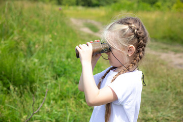 Little girl with binocular looking for the right path in summer park outdoor. Child exploring forest nature and environment on sunny day during outdoor ecology