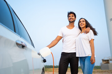 save world save life. World Environment Day. Hispanic couple male female driver electric car holding electrical plug connector to charge the batteries hybrid car at home or charging station