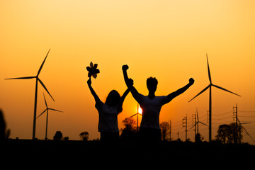 silhouette Hispanic brazillian couple standing together in front of wind turbine. Wind turbines for...