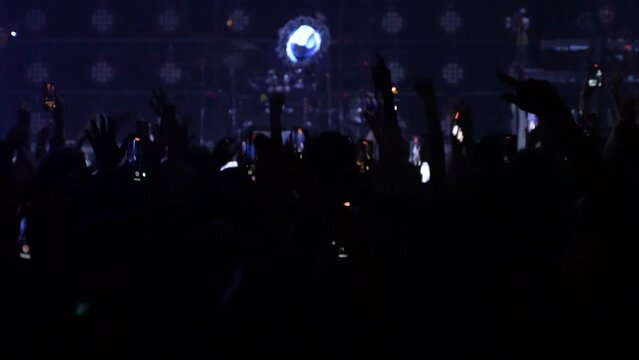 Slow motion unrecognizable fans hands dancing at a concert or festival party. Silhouettes of concert crowd in front of bright stage lights. High quality 4k footage