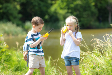 Two children boy and girl 5-6 years old with a backpack talking on a walkie-talkie in the forest,...
