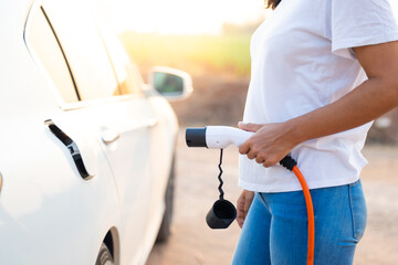 World Environment Day. save world save life concept. Hispanic woman driver electric car holding electrical plug connector to charge the batteries hybrid car at home or charging station.
