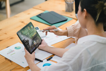 Two businesspeople or an accountant team are analyzing data charts, graphs, and a dashboard on a laptop screen in order to prepare a statistical report and discuss financial data in an office.