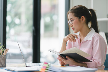 An Asian businesswoman is using a laptop computer and working with a calculator and documents, conducting financial planning for investments and analyzing the financial report.