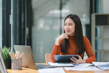 Happy smiling business woman working with laptop computer with paperwork at desk in a modern office, business finance technology concept.