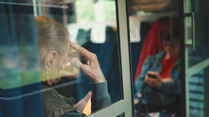 Closeup, Pensive elderly man uses mobile phone while traveling in train coupe, view through glass