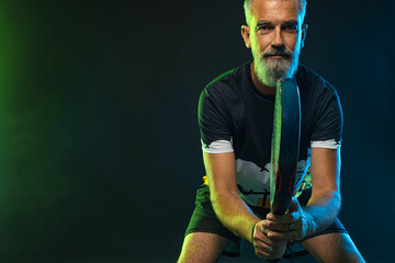 Old padel tennis player with racket. Man athlete with paddle tenis racket on court with neon colors. Sport concept. Download a high quality photo for the design of a sports app or betting site.
