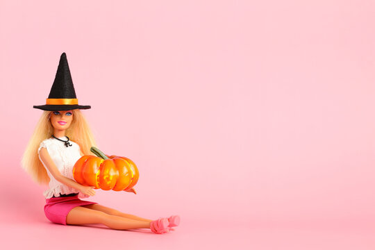 Grodno, Belarus - August 07, 2023: Barbie doll in witch's hat holding orange pumpkin in her hands on pink background