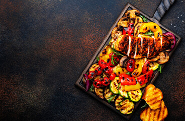 Grilled chicken and vegetables. Bbq party. Colorful paprika, zucchini, eggplant, mushrooms, tomatoes, onion and rosemary, served on wooden cutting board, brown table background, top view