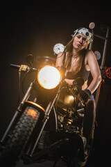 Naklejka premium Girl motorbiker in the bandana and black top posing on the old retro motorbike.